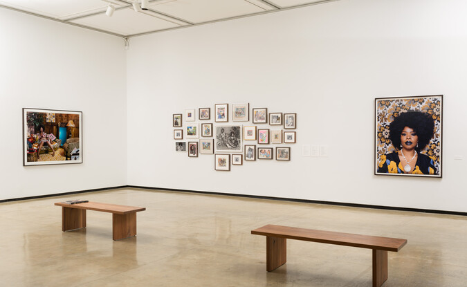 Installation view of a gallery with photographs and montage of 2-dimensional works with 2 wooden benches on the floor