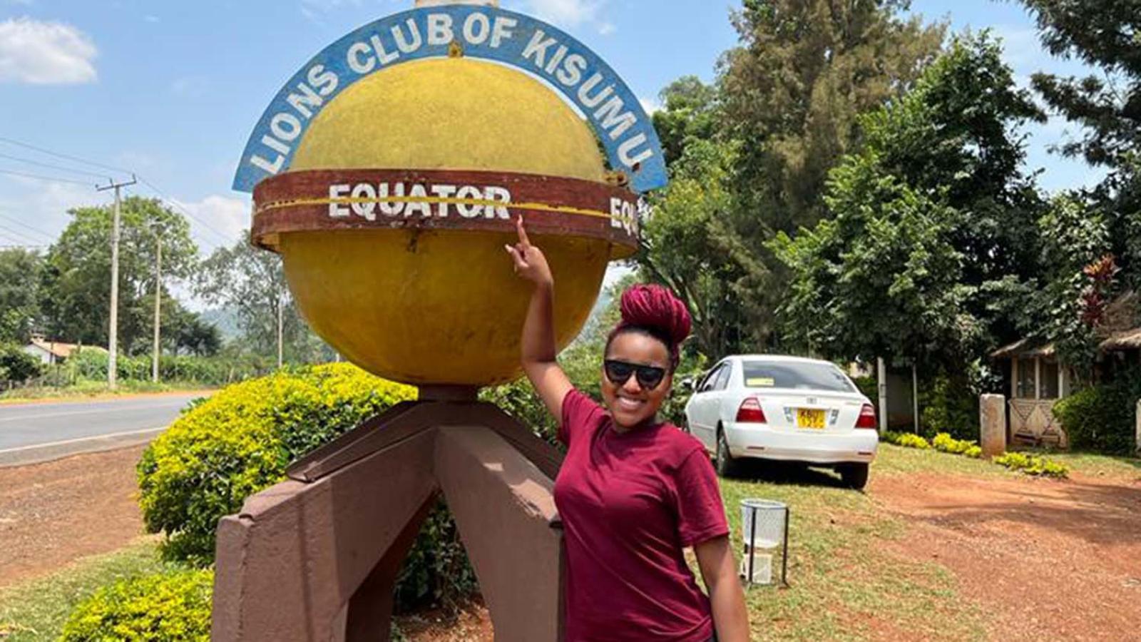 Kiya Henderson standing with globe statue marking the equator in Kenya.