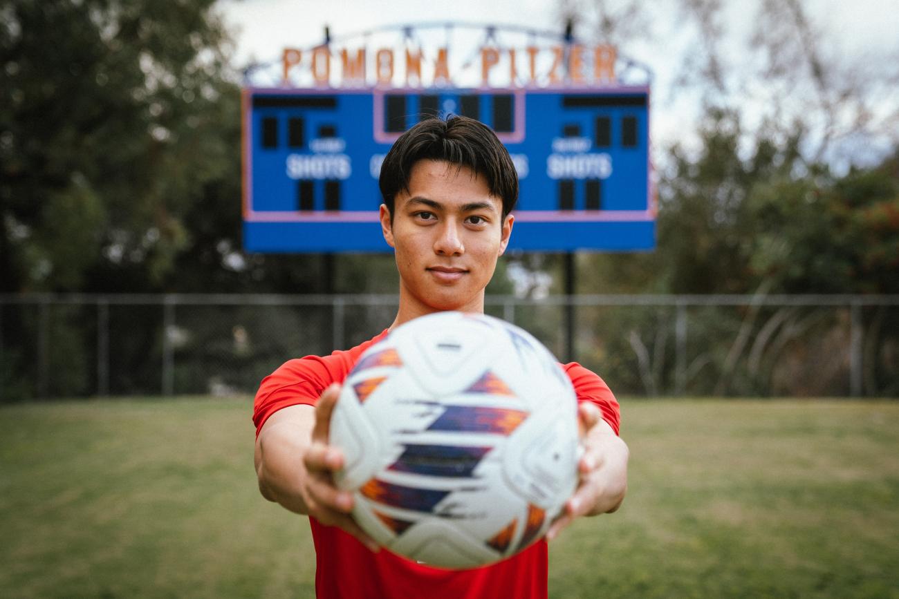 Kyle Lau holds ball in front of Pomona-Pitzer scoreboard