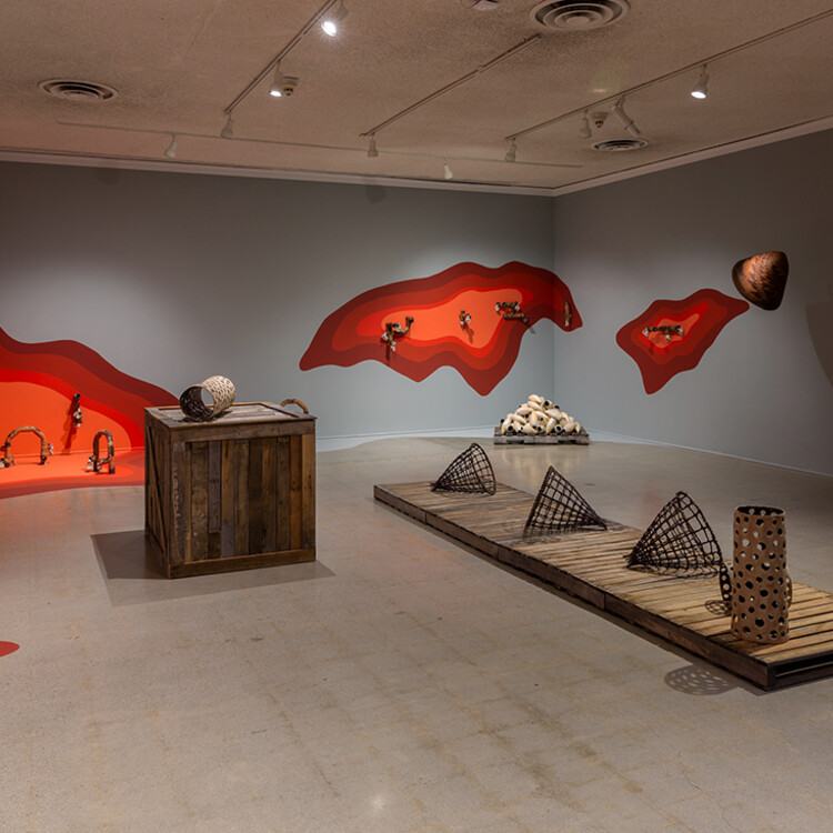 Installation view of ceramic works on wood platforms and wavy red paintings on wall and floor from an angle