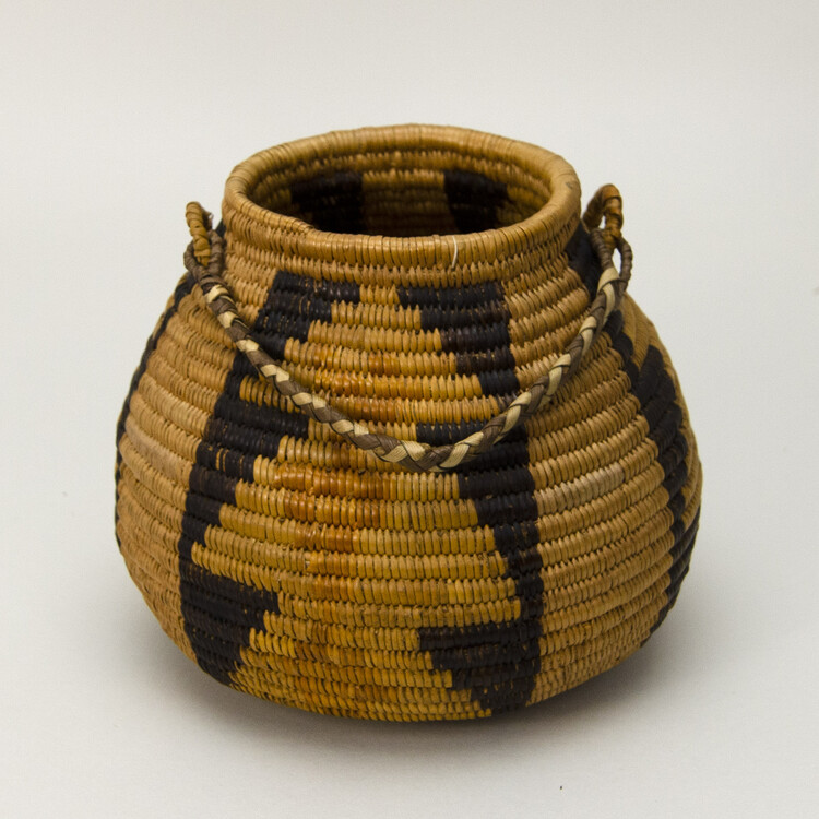 Ring necked basket with a flat base and braided handle. Made with coiled construction. Three bands of black, tan and buff geometric designs on buff.