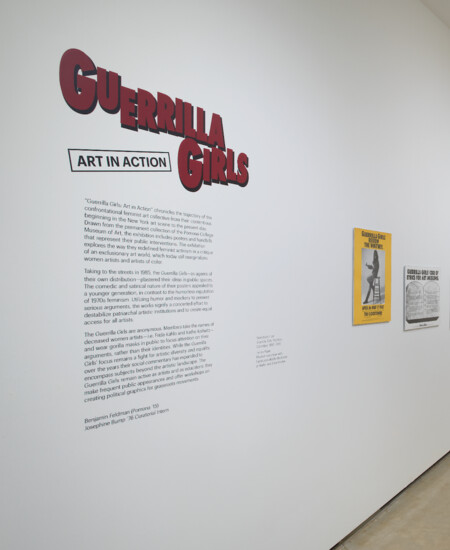Installation view of Guerrilla Girls exhibit with graphic vinyl lettering on the wall with 2-dimensional posters and artworks