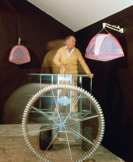 A person in motion on cycle like contraption maneuvering from tent container hanging on walls