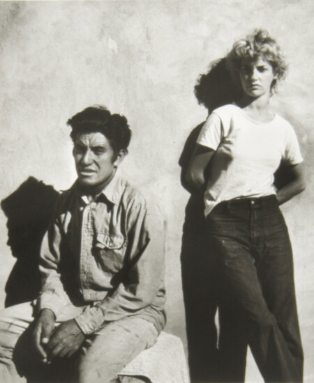 A man sitting down and a woman standing up next to him outdoors on sunny day