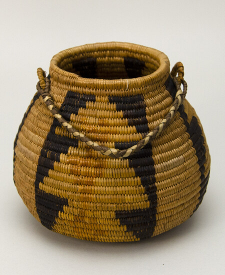 Ring necked basket with a flat base and braided handle. Made with coiled construction. Three bands of black, tan and buff geometric designs on buff.