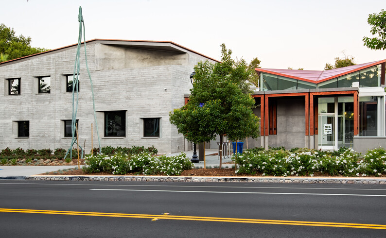 street view of a building with a tall sculpture in front adjacent to palm trees