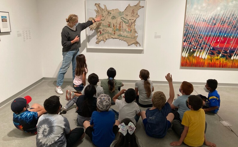 a group of kids looks at person stands and points at a painting