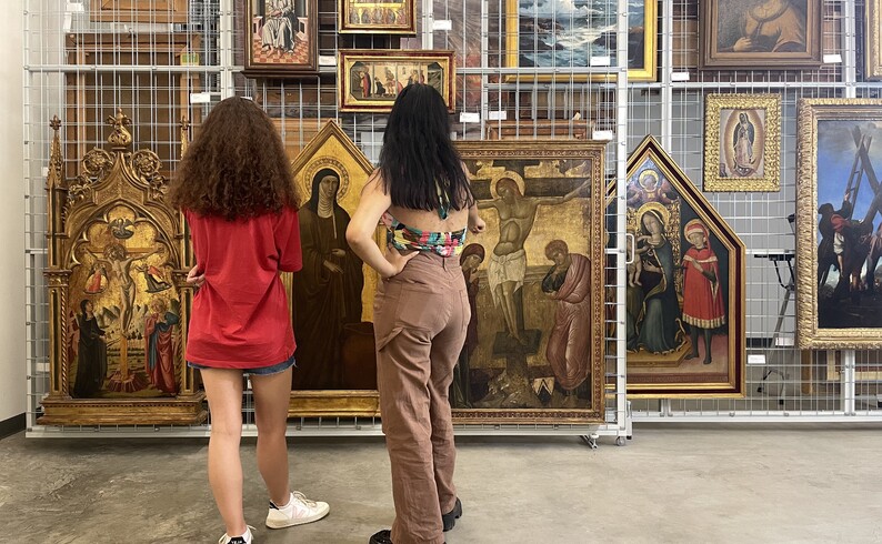 two people look at paintings on a rack