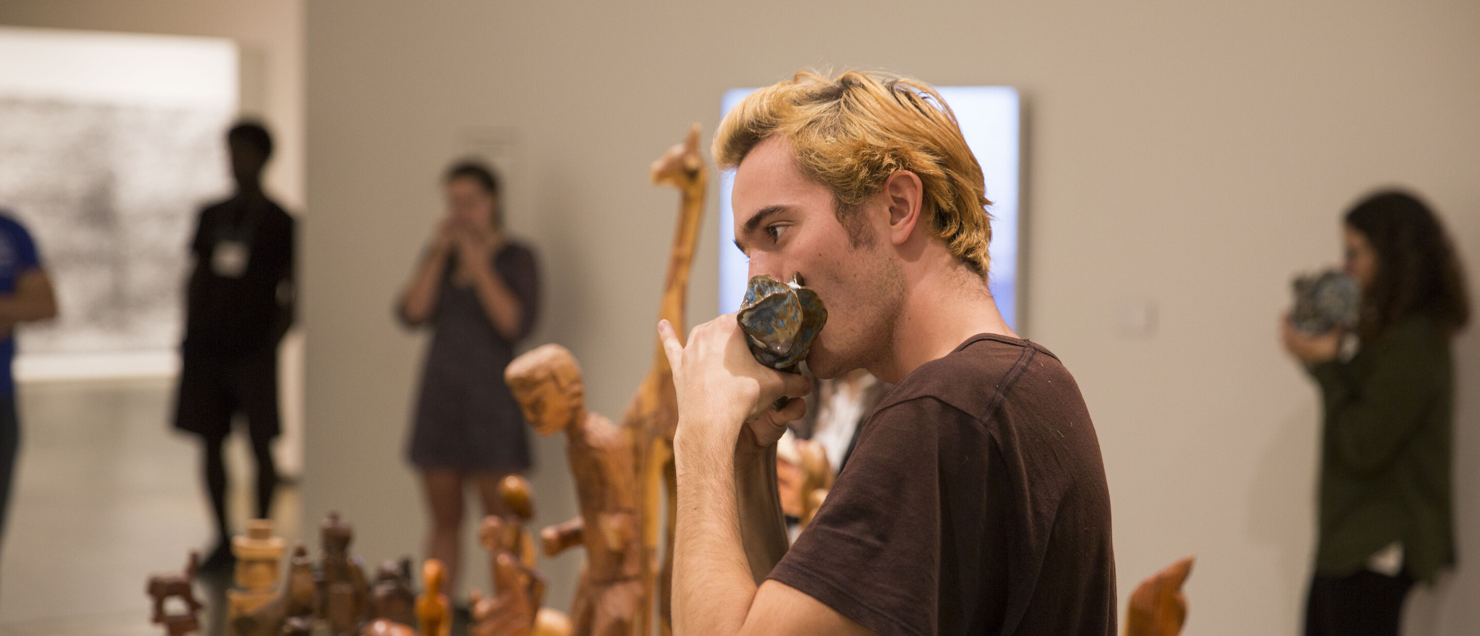 Student blowing into a ceramic instrument with others doing the same behind 