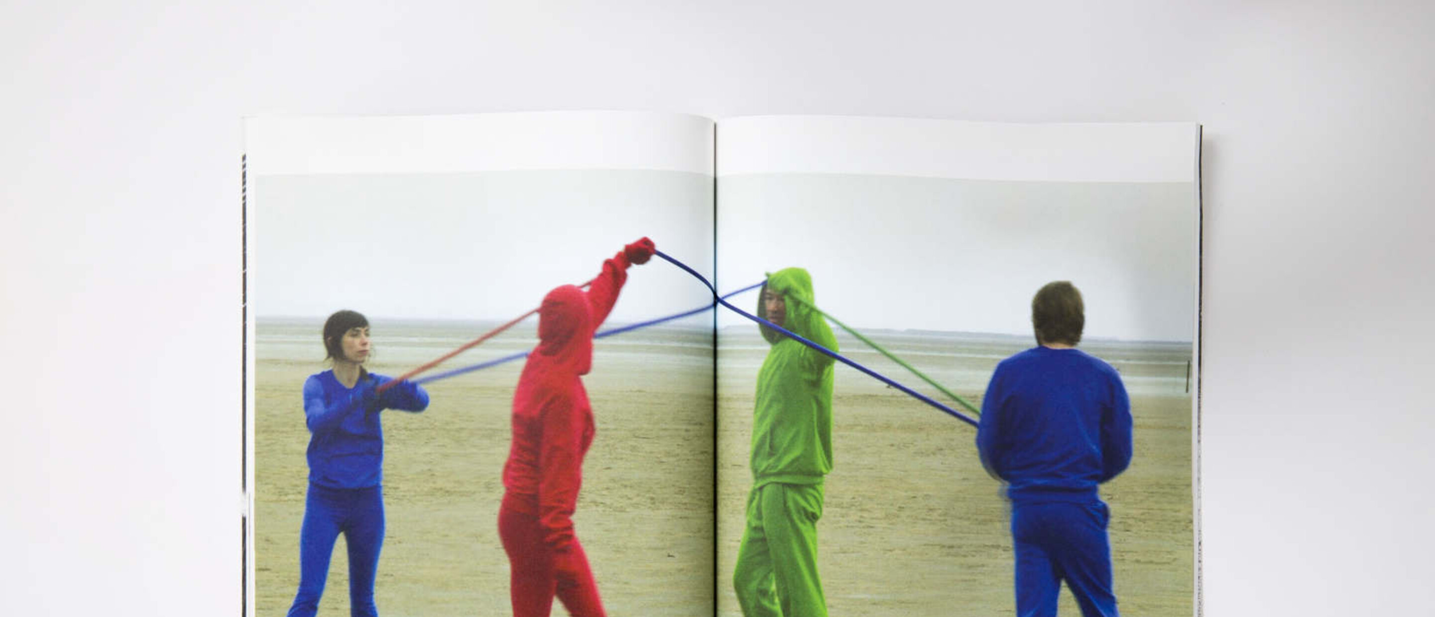Catalogue spread showing photograph of 4 figures in primary colored outfits connected by thread