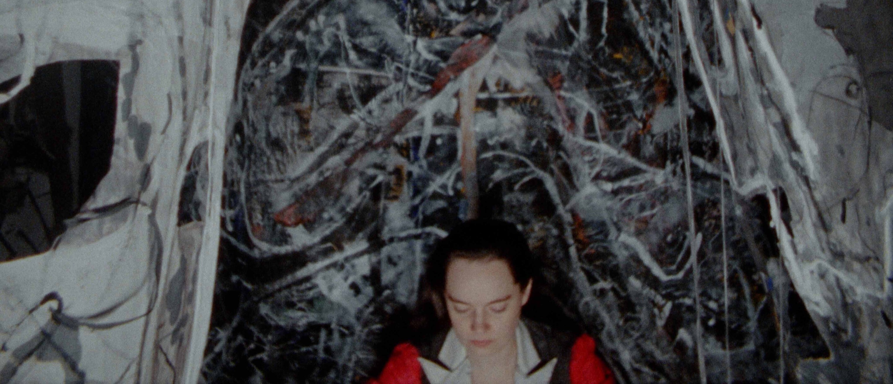 woman with red jacket sitting in front of abstract painted canvases