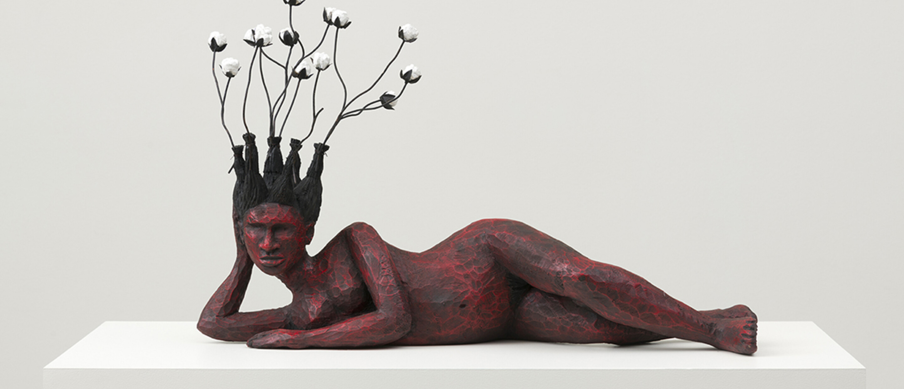 sculpture of reclining woman painted red with cotton balls attached to her hair