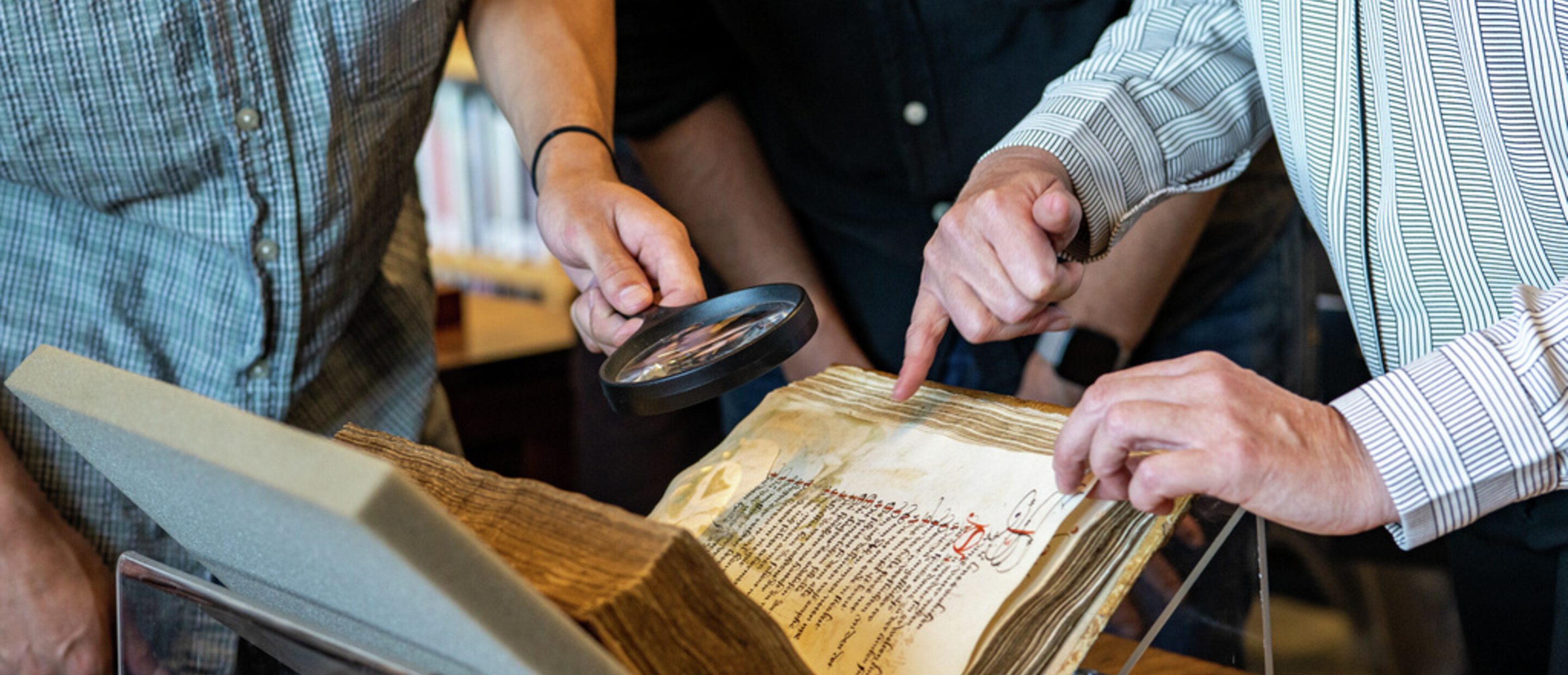 peoples hands pointing to and using magnifying glass to look at a manuscript