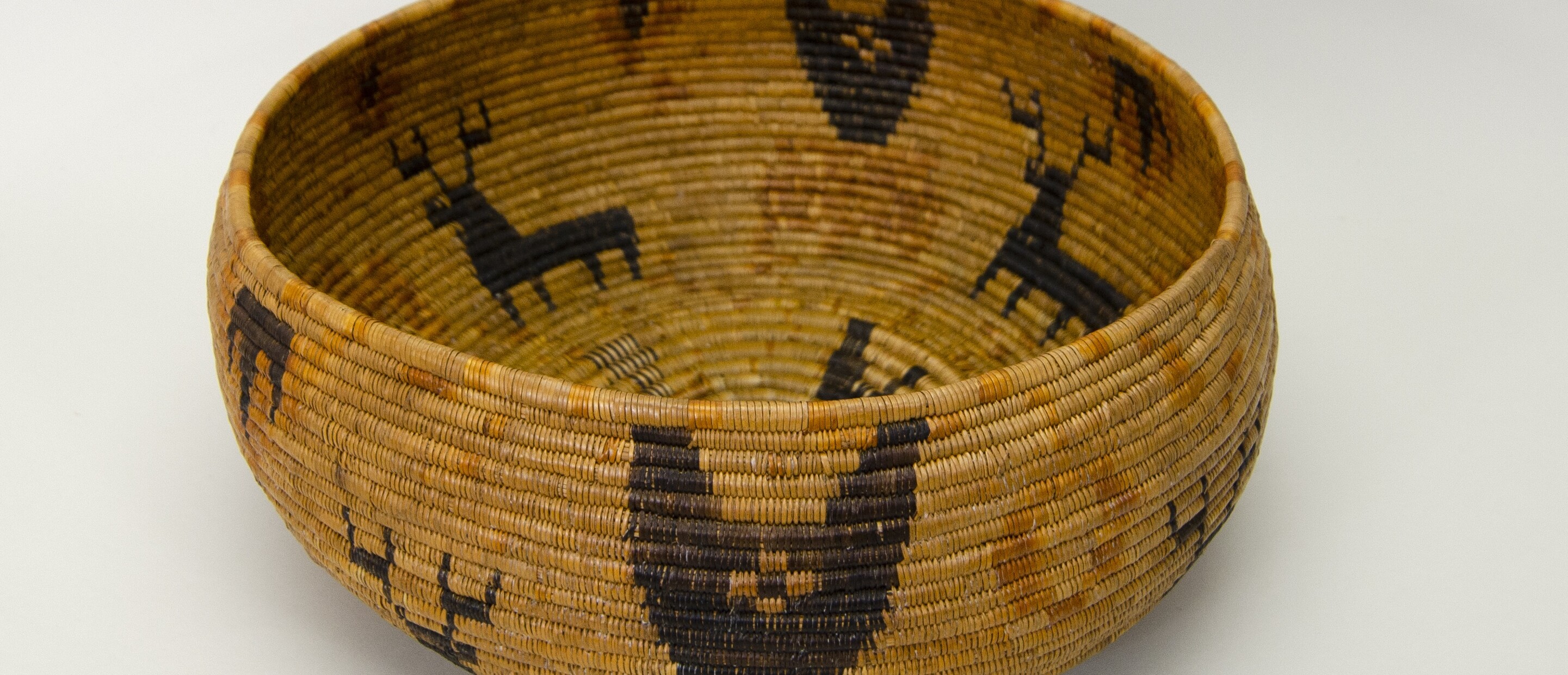 Restricted hemispherical basket with a flat base. Coiled construction. Four black deer with antlers on buff background.