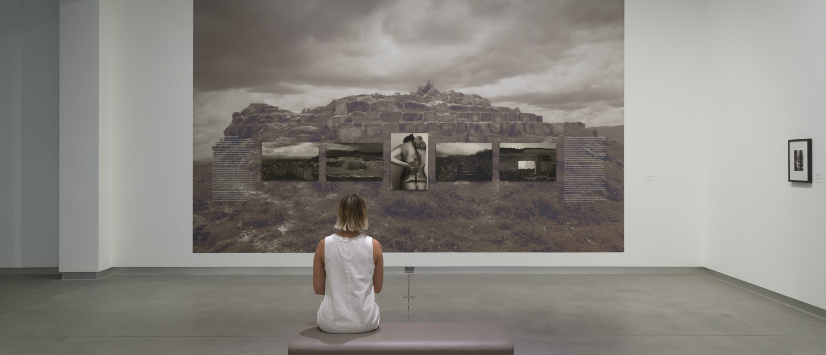 woman sits on bench in gallery in front of larger gray photograph on the wall