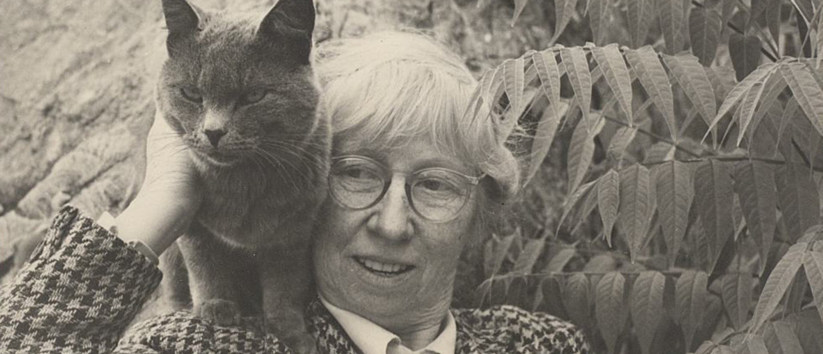 Individual in glasses with black cat against foliage background