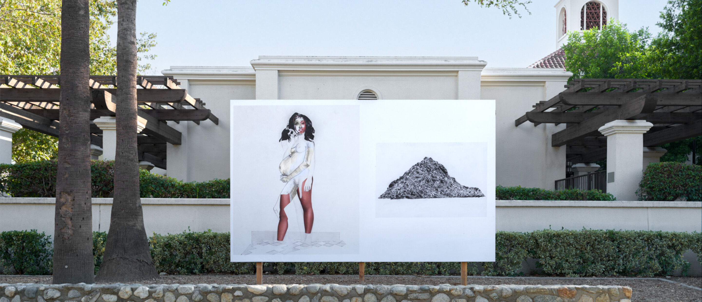 white billboard behind short rock wall, in front of a white building, and two trees