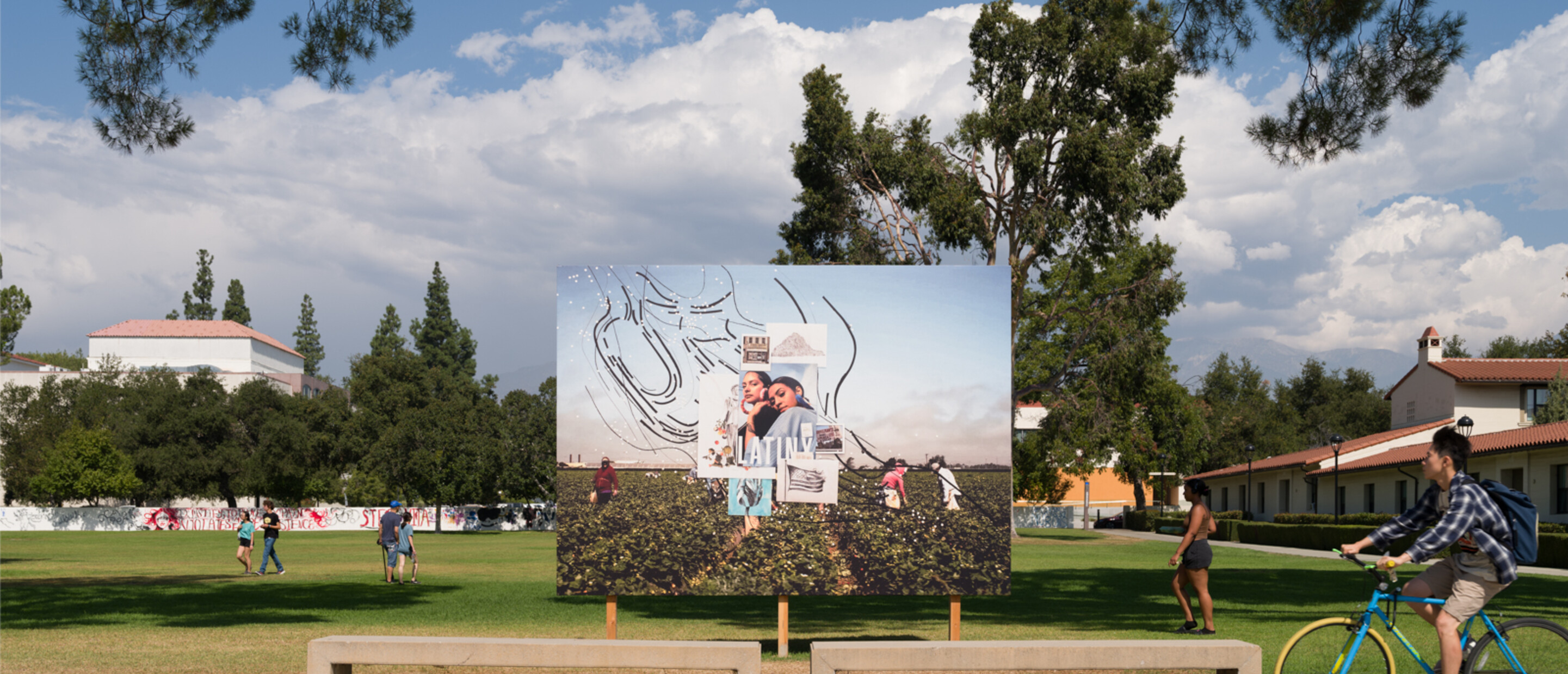 billboard in front of field with trees and clouds. a person riding a bike is about to pass in front of the scene