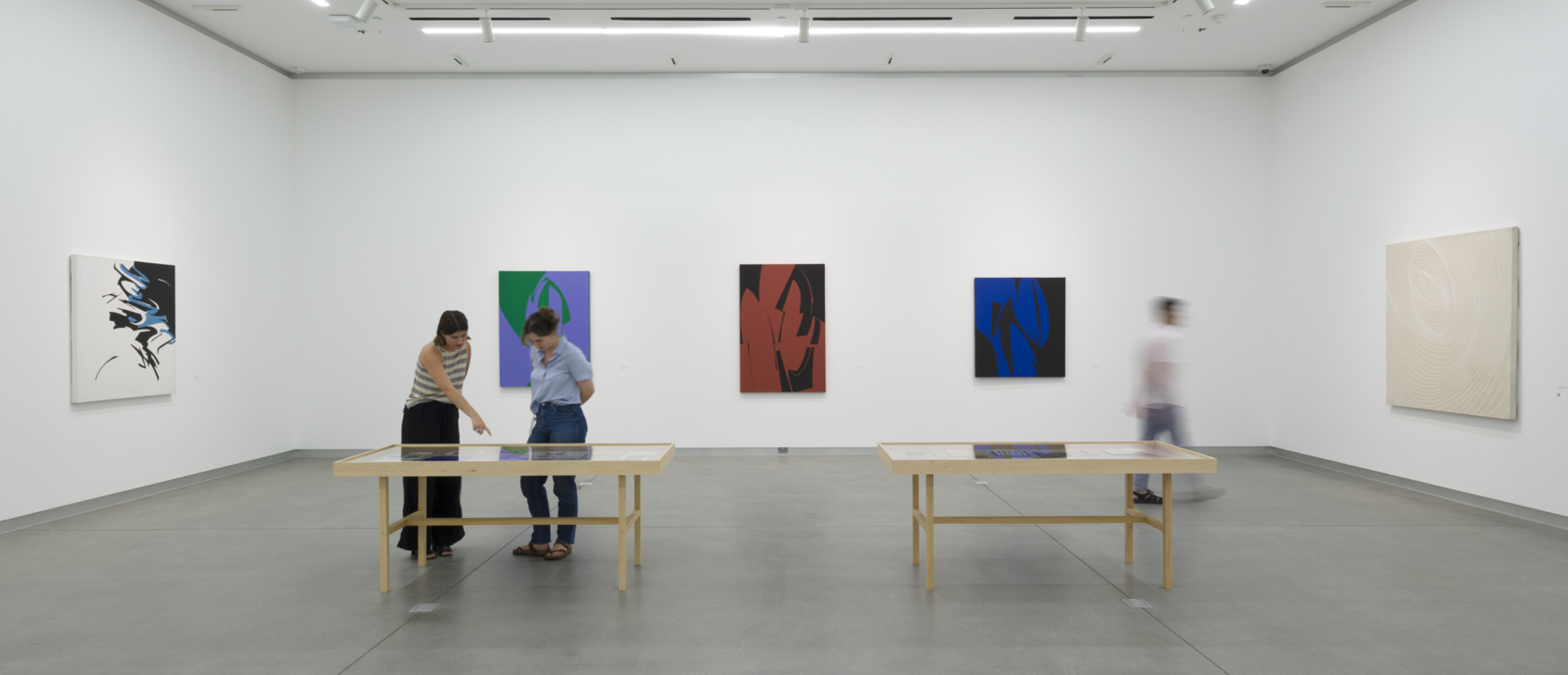 gallery with three people looking at art on tables and walls