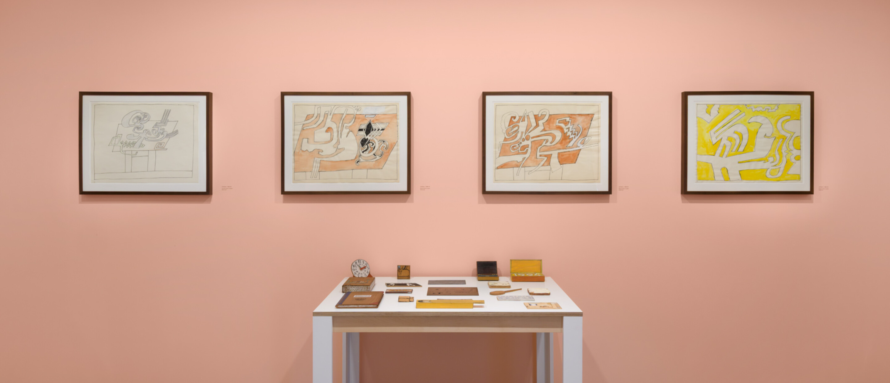 wide shot of artworks on pink wall and a replica of a drawing table relief in foreground