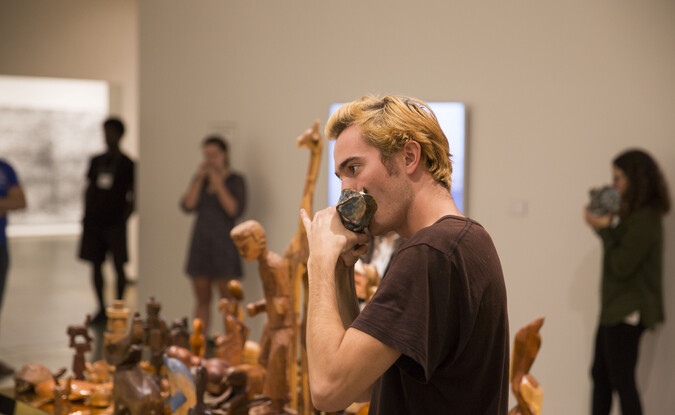 Student blowing into a ceramic instrument with others doing the same behind 