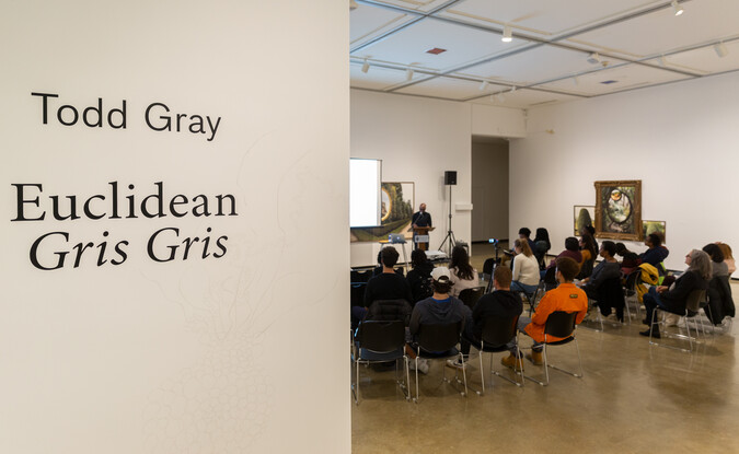 View into a gallery for a public lecture with audiences in seats with a speaker up front
