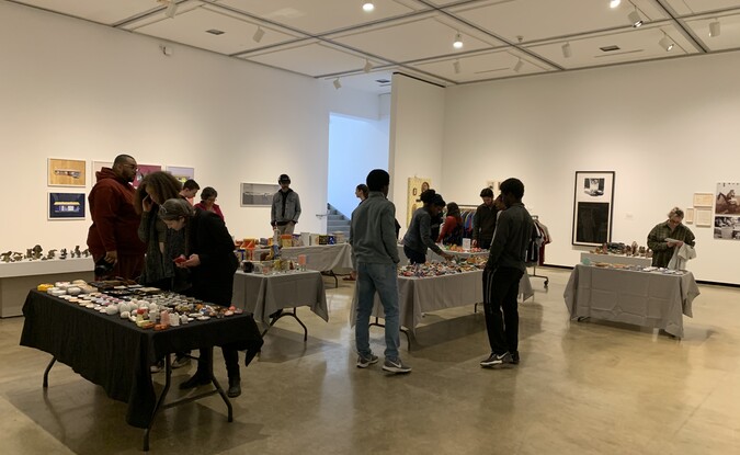 Inside a gallery a pop-up shop with lots of items set up with people walking around
