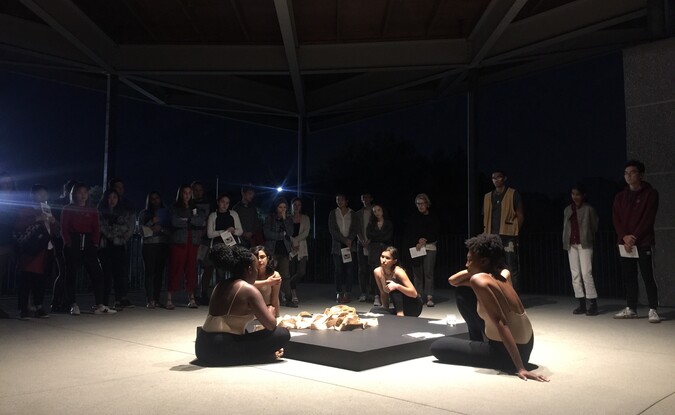 4 women sitting around a square block with an audience behind them during a performance