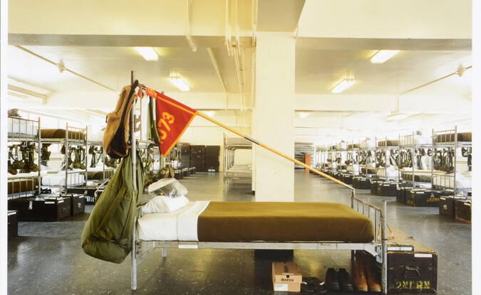 Empty bed with flag overhead with rows of beds behind