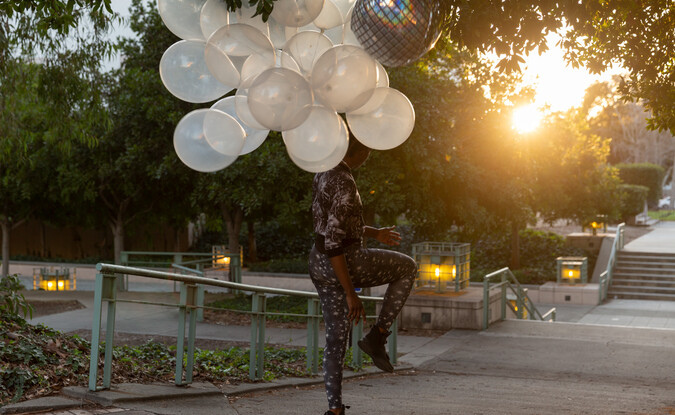 Dancer performer outdoors with silver latex and mylar balloons tied to them 