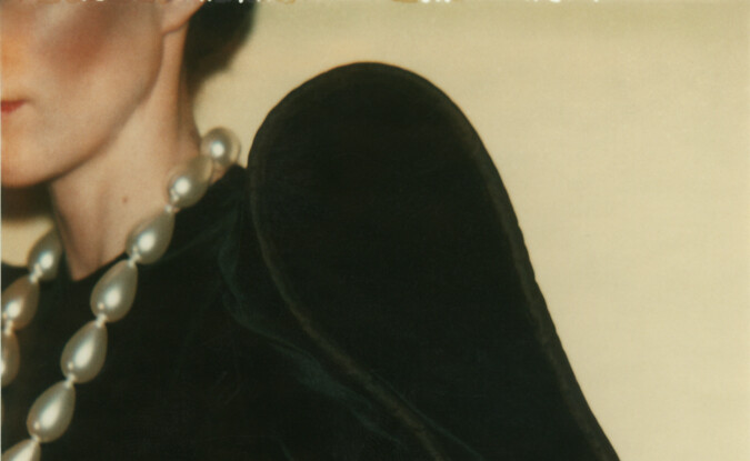 Faceless portrait of individual with pearl necklack on velvet high shoulder top