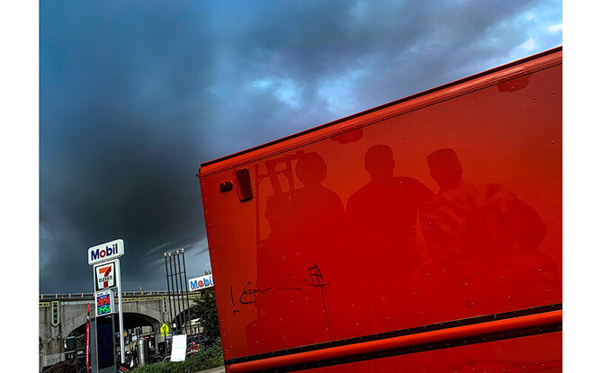 Reflections of individuals against red surface outdoors near gas station