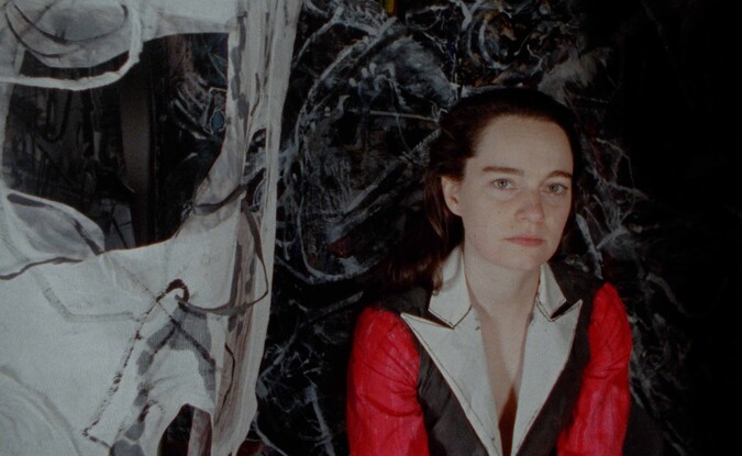 woman in red, black, and white jacket in front of dark painted canvases