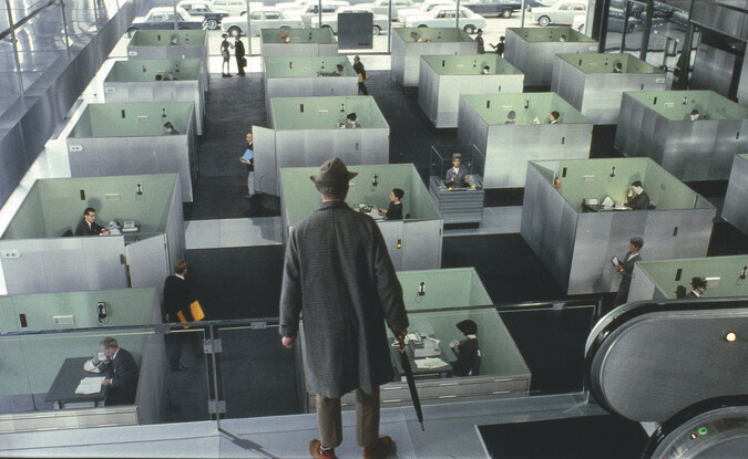 man in top hat and long coat looking down at rows of cubicles