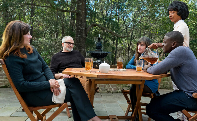 Group of people sitting around on wooden table outdoors being served drinks