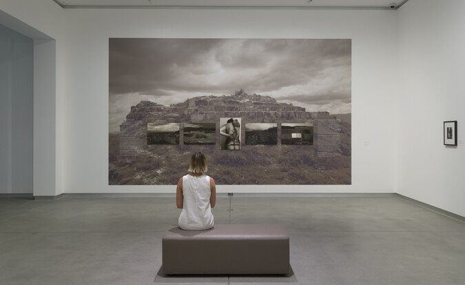 woman sits on bench in gallery in front of larger gray photograph on the wall