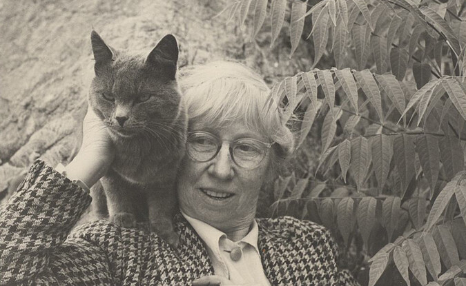 Individual in glasses with black cat against foliage background