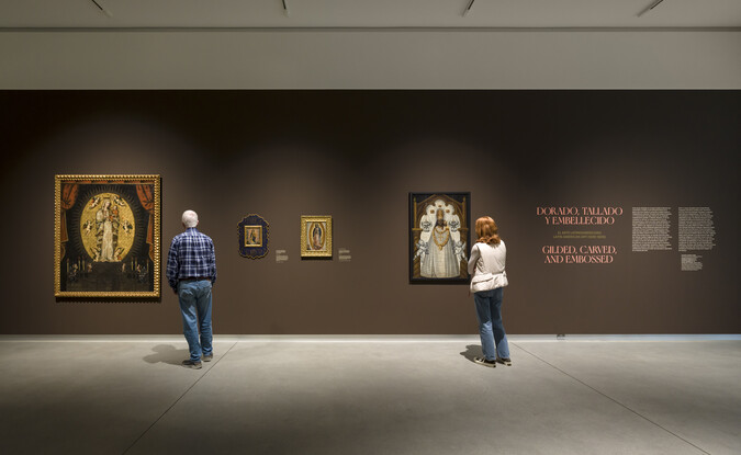 two people look at brown gallery wall with multiple paintings