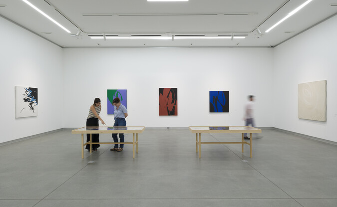 gallery with three people looking at art on tables and walls