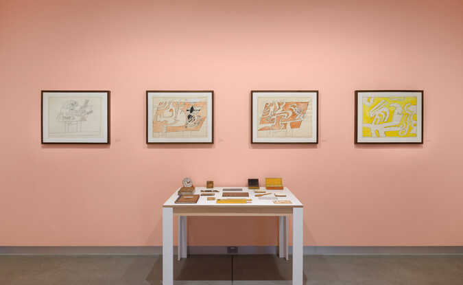 wide shot of artworks on pink wall and a replica of a drawing table relief in foreground