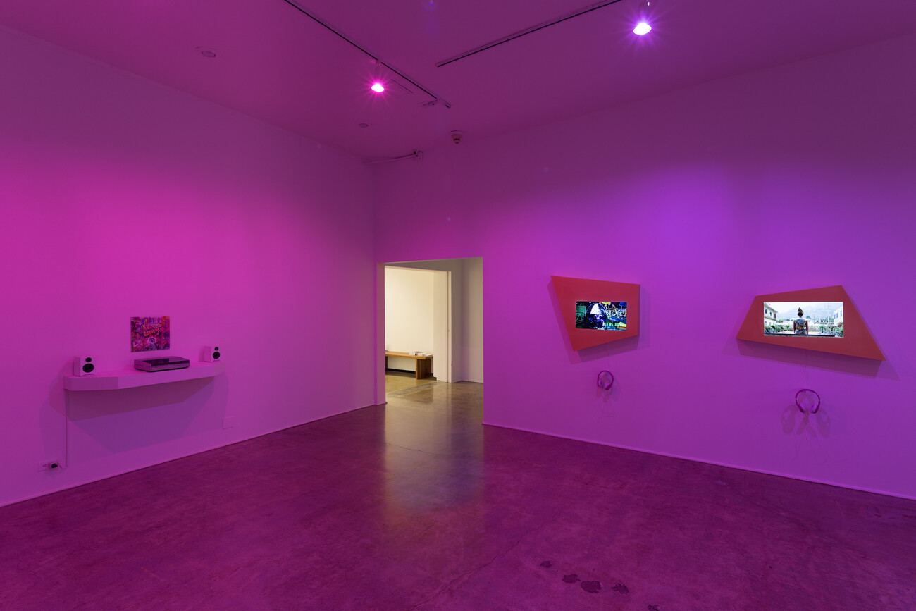 Installation view of gallery pink lighting with monitors framed in trapezoid shapes