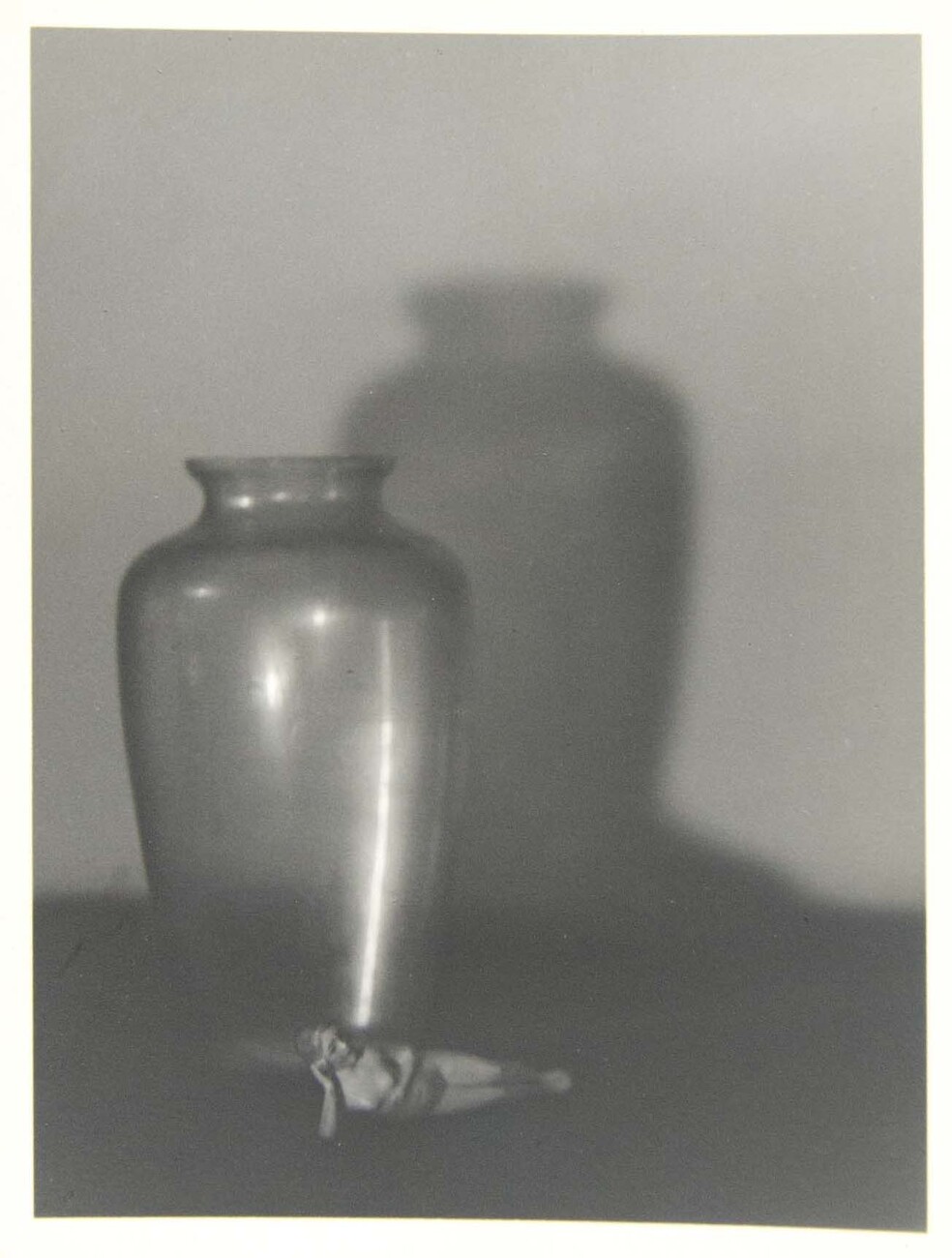 Black and white portrait of a vase and shadow with figurine adjacent to glass jar