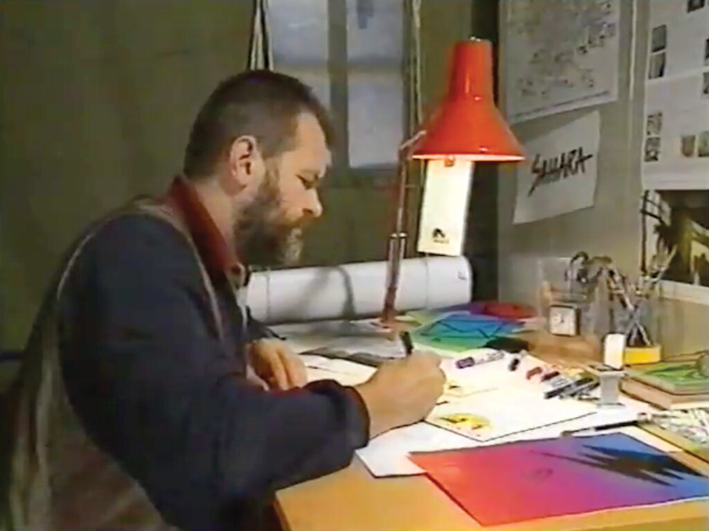 Person at desk with pen and paper under desk lamp