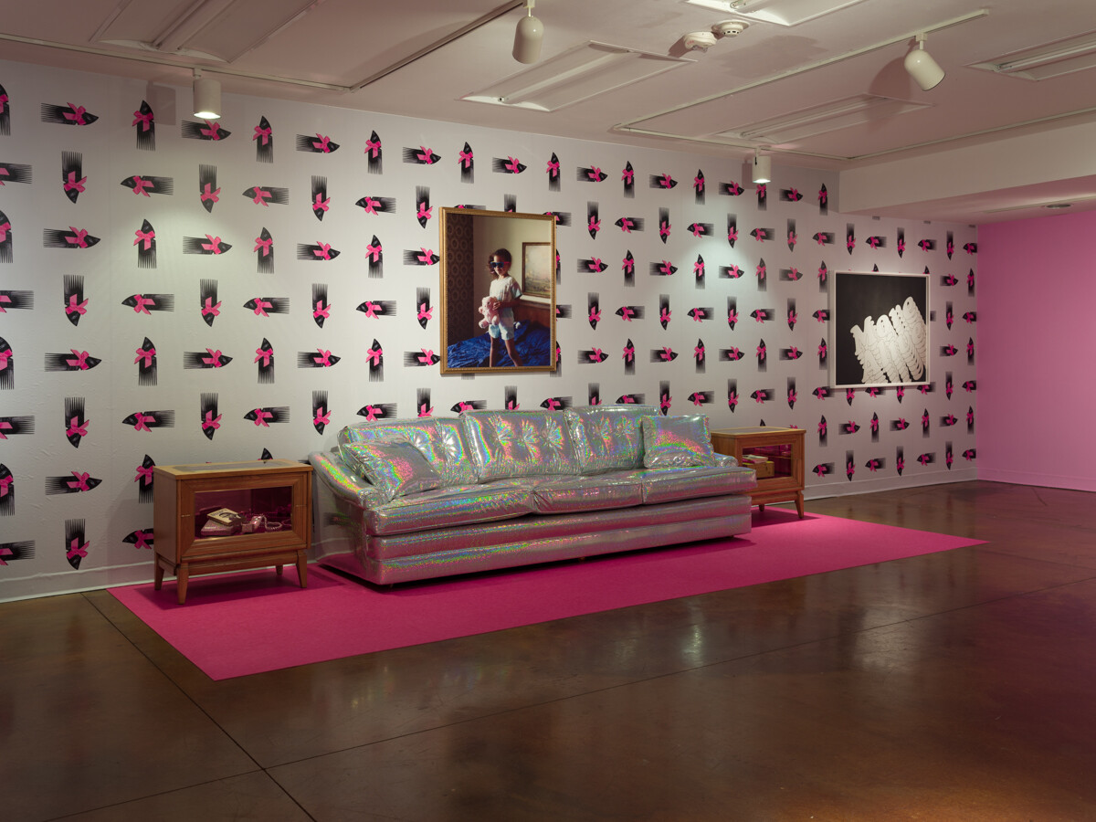 Art installation with works on wall and 3-dimensional works including silver couch and side tables