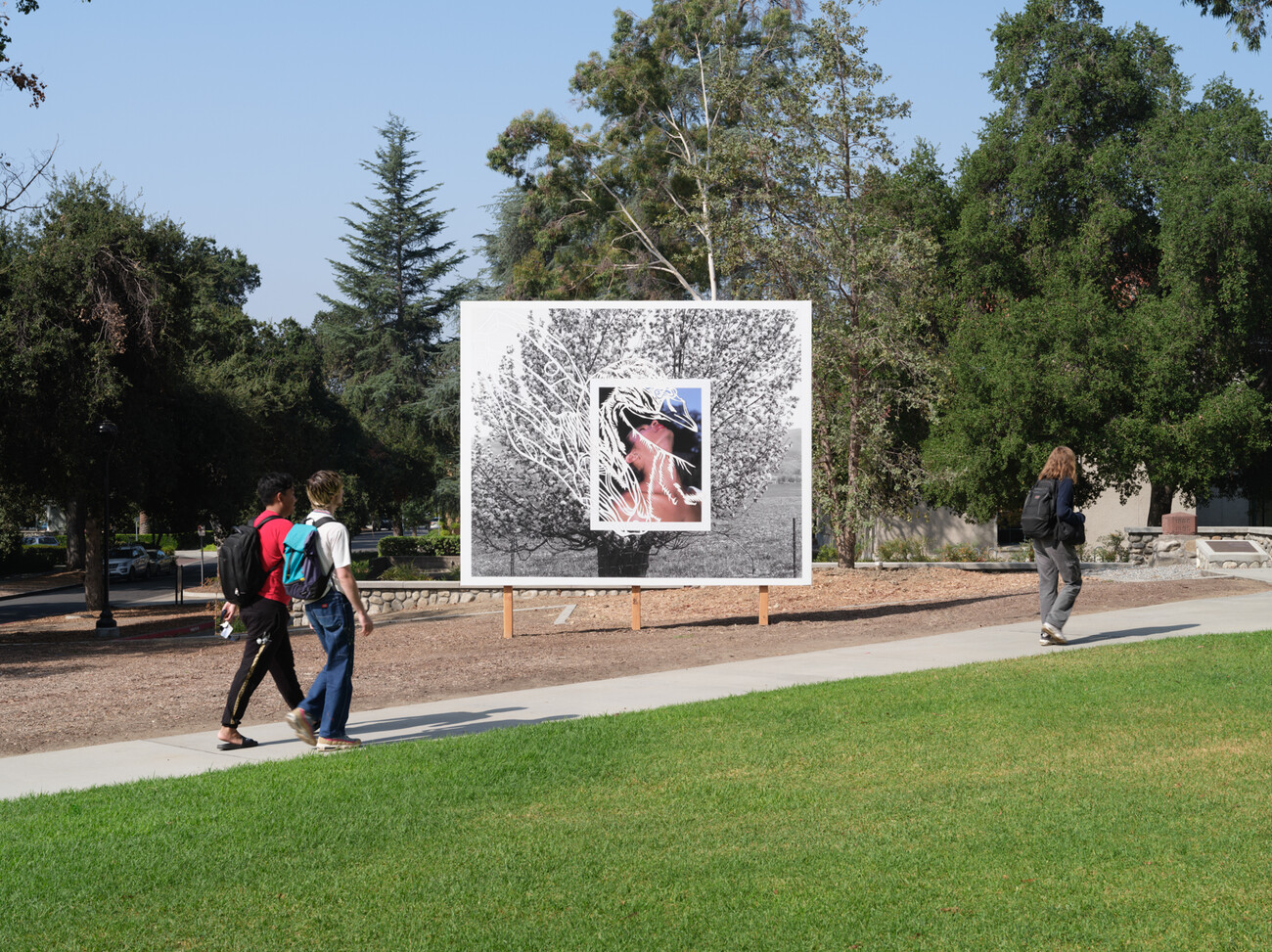 three people walk down path with billboard in the background