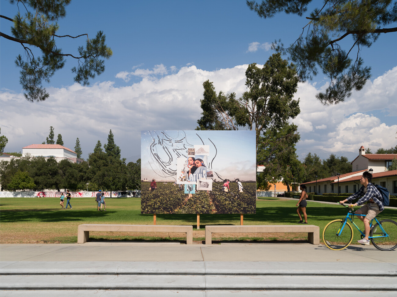 billboard in front of field with trees and clouds. a person riding a bike is about to pass in front of the scene