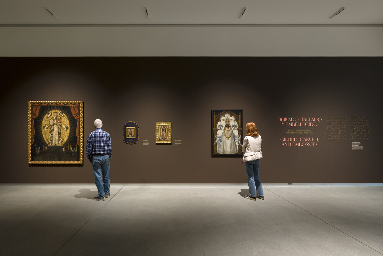 two people look at brown gallery wall with multiple paintings