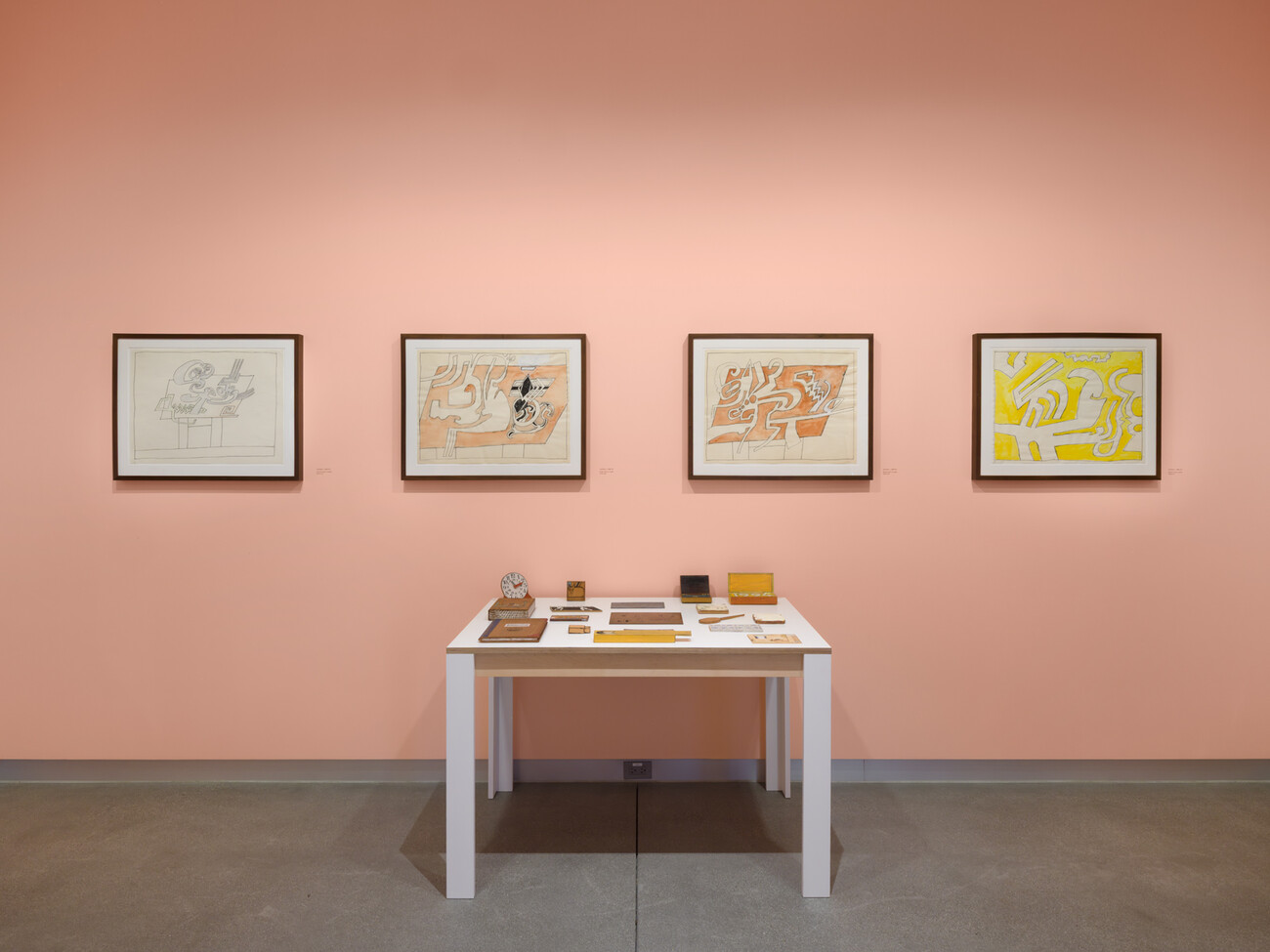 wide shot of artworks on pink wall and a replica of a drawing table relief in foreground