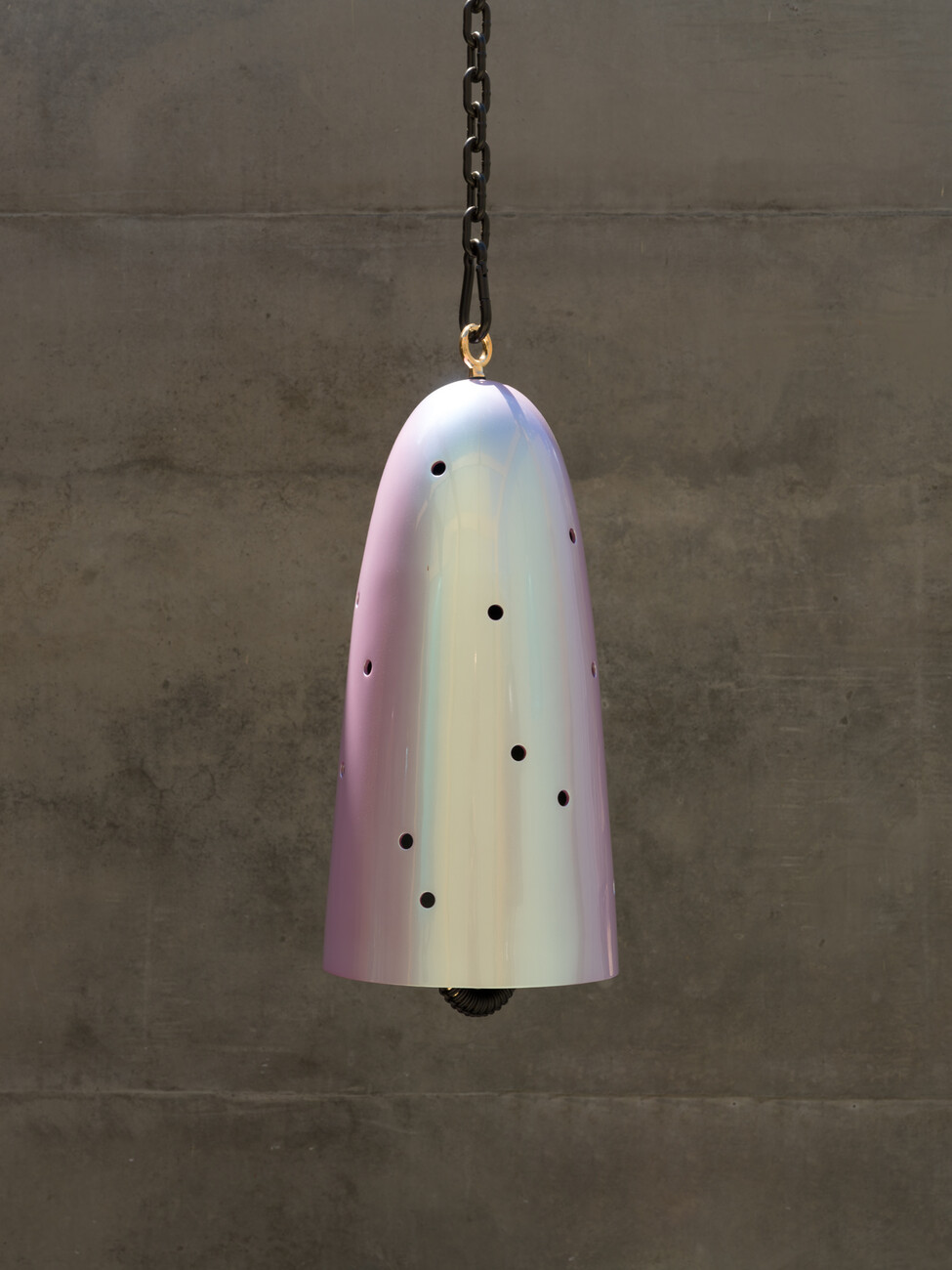 single bronze bell hanging from a chain, with outdoor concrete wall in the background