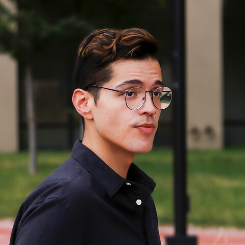 Short haired person with round glasses sitting in a courtyard